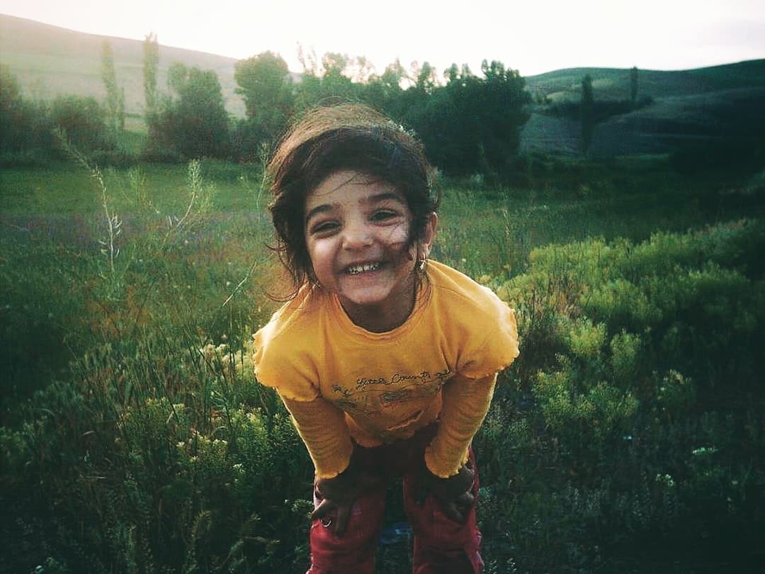 A young child smiles in a sunlit grassy field.